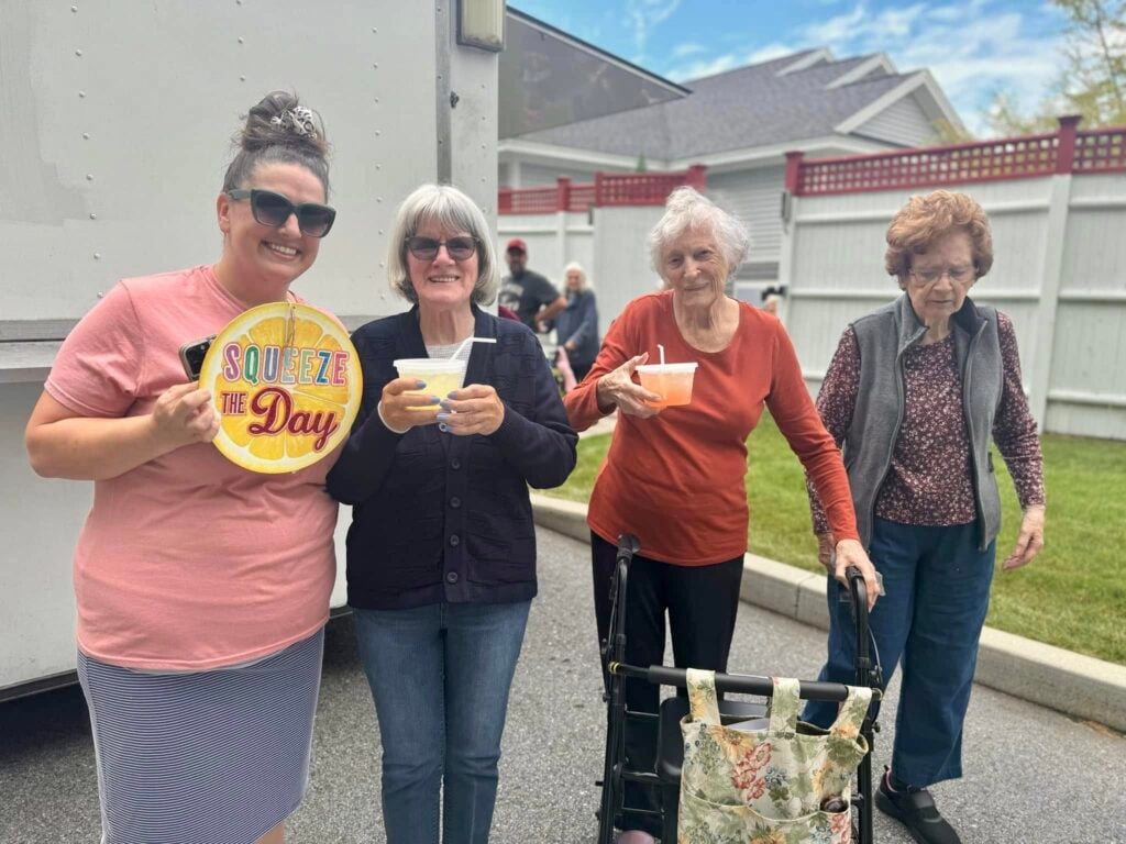Four women stand together displaying cups of lemondae and a lemon-shaped sign reading Squeeze the Day.
