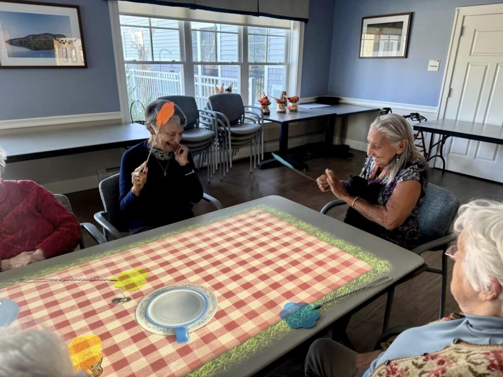 Two older women interact with a Tovertafel table while holding fly swatters.