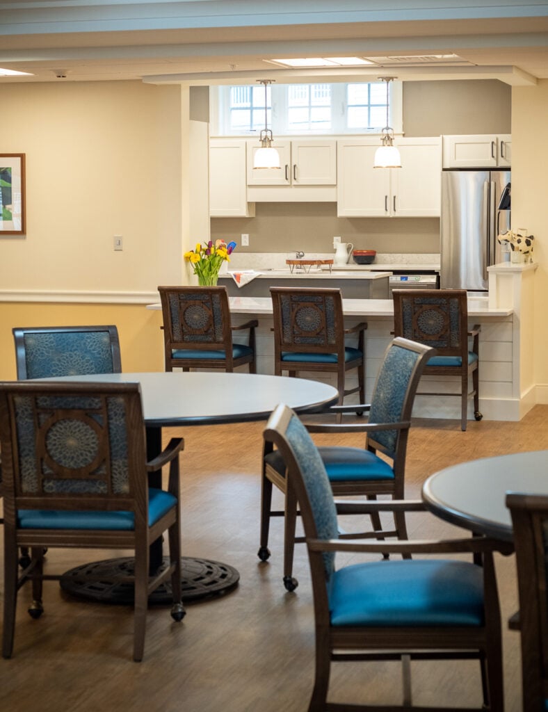 Lounge area facing a kitchen with chairs and tables.