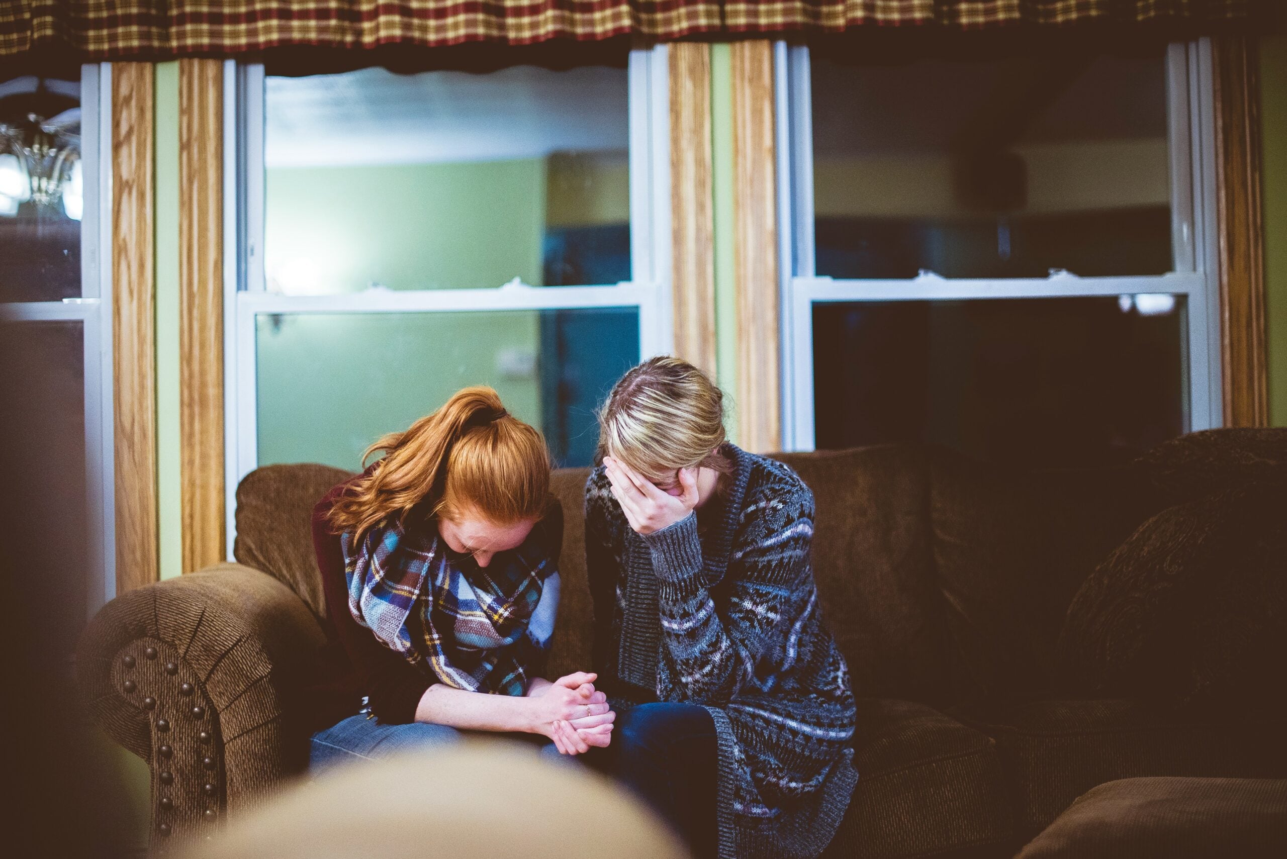 Two people sitting on a brown couch with their heads bowed in a sad manner.